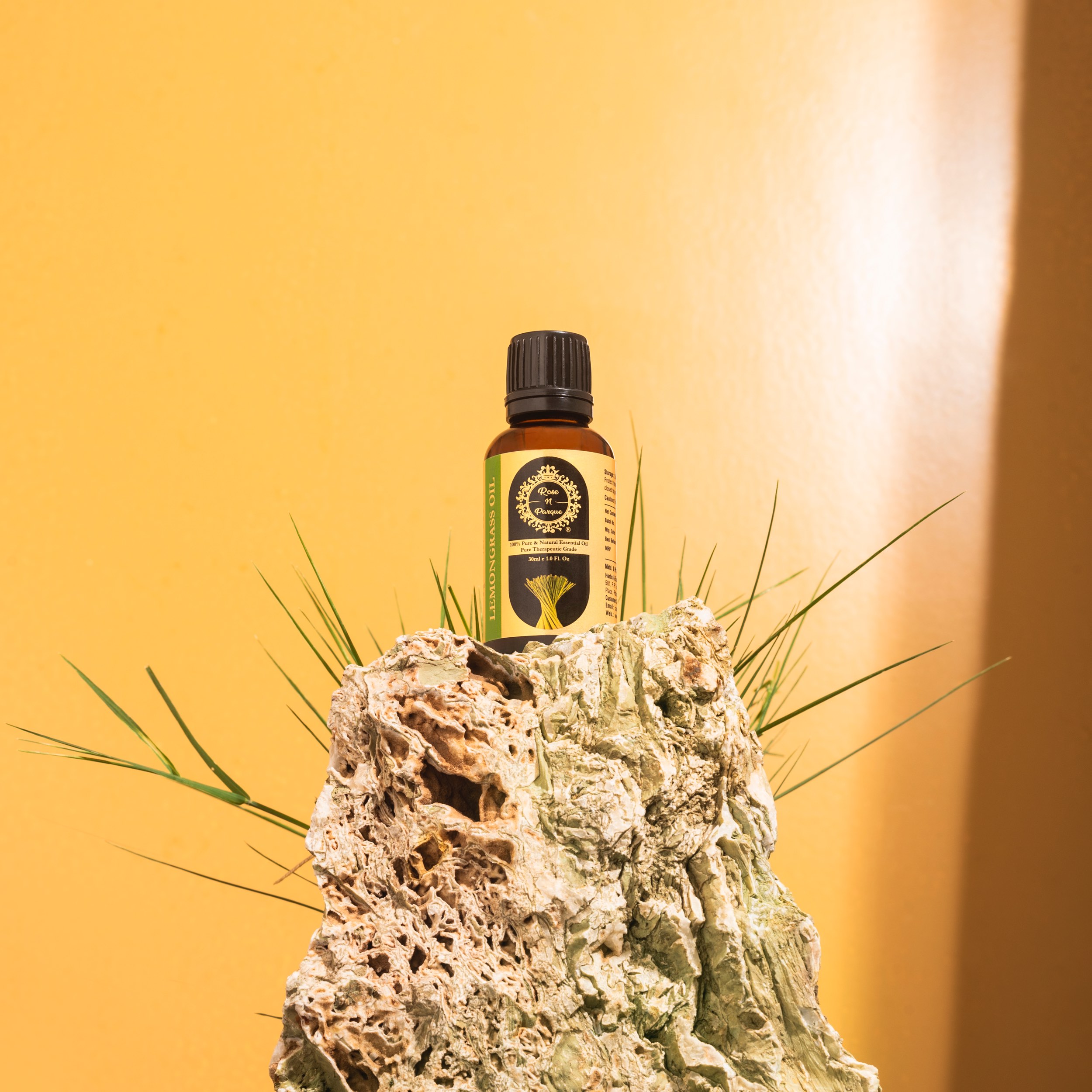 Brown essential oil bottle with a black cap placed on a textured rock against a yellow background.