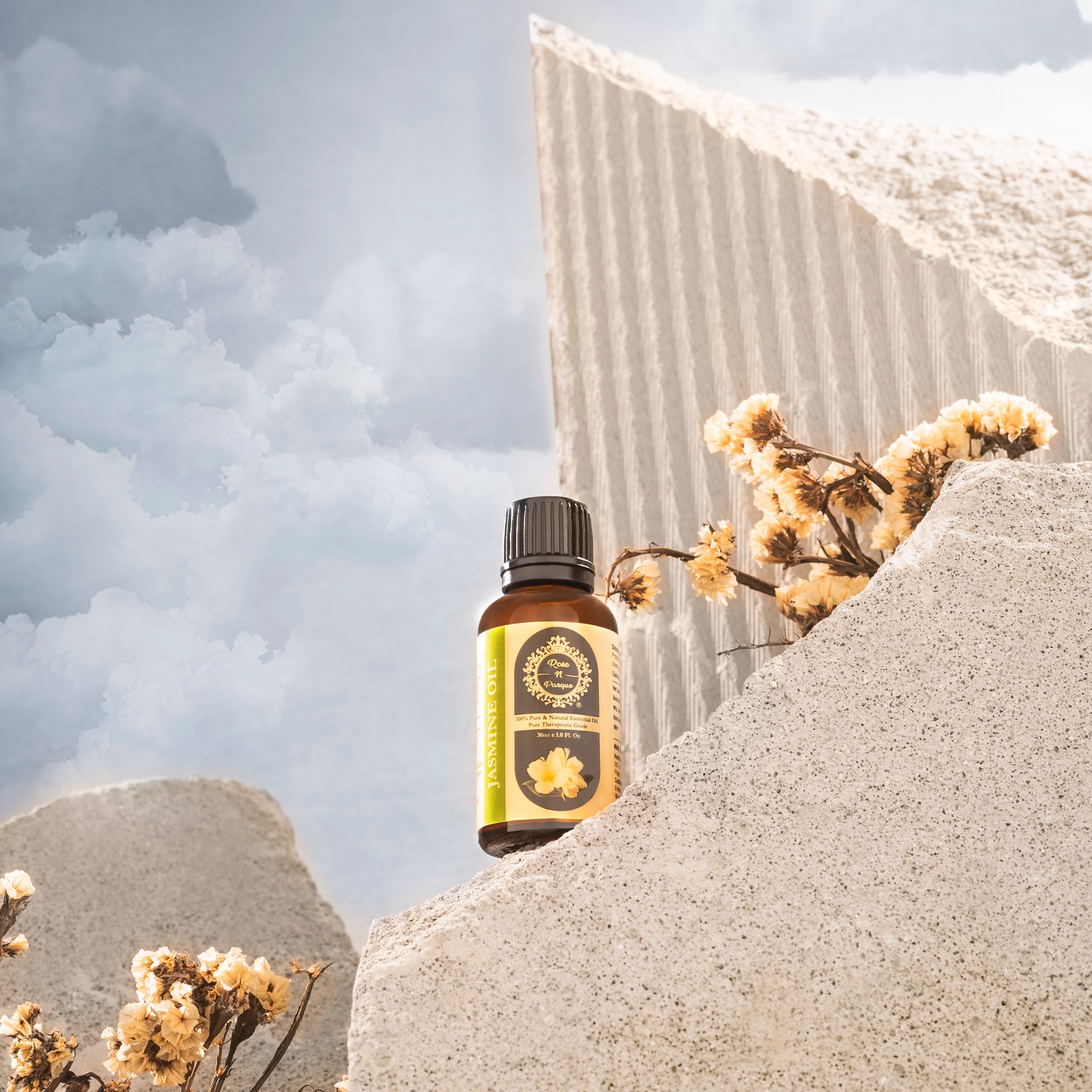 Brown glass bottle of essential oil placed on textured stone with dried flowers.