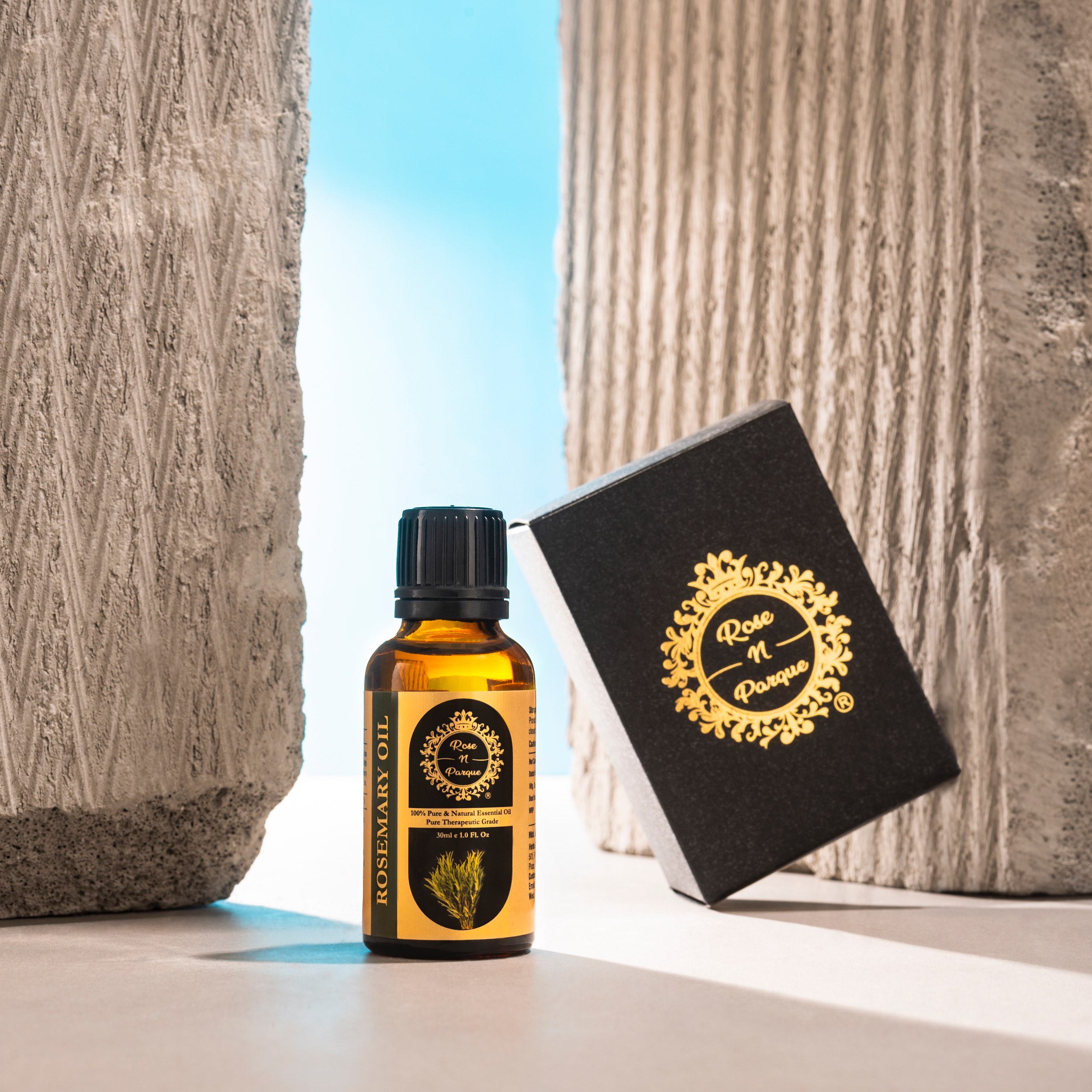 Brown glass bottle of rosemary essential oil next to its black packaging on a light surface.