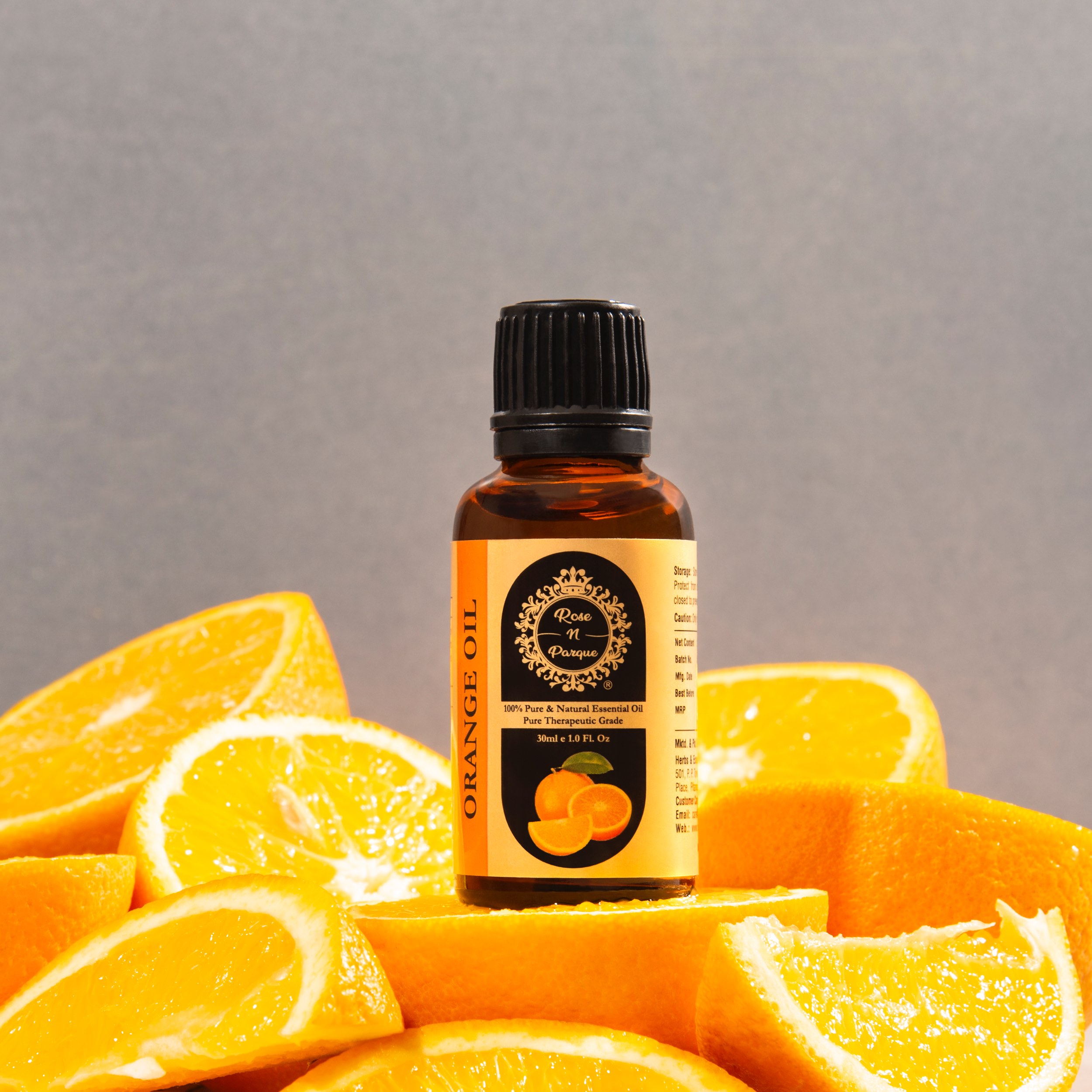 Amber bottle of orange essential oil with a black cap placed on sliced oranges.