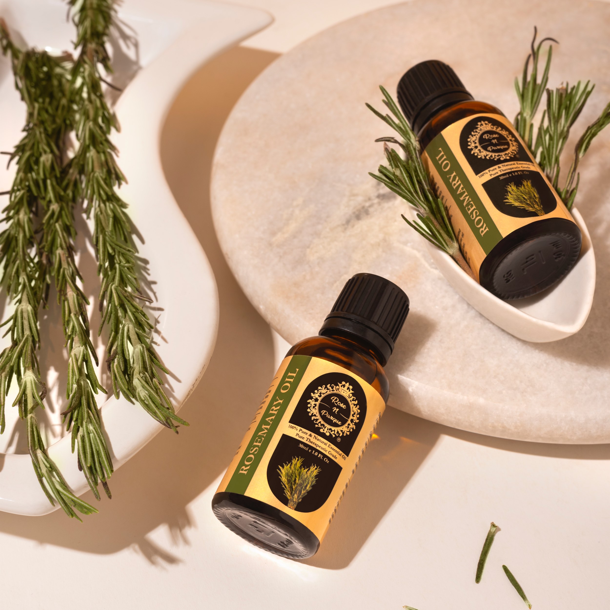 Two bottles of rosemary essential oil placed on a light surface with rosemary sprigs.