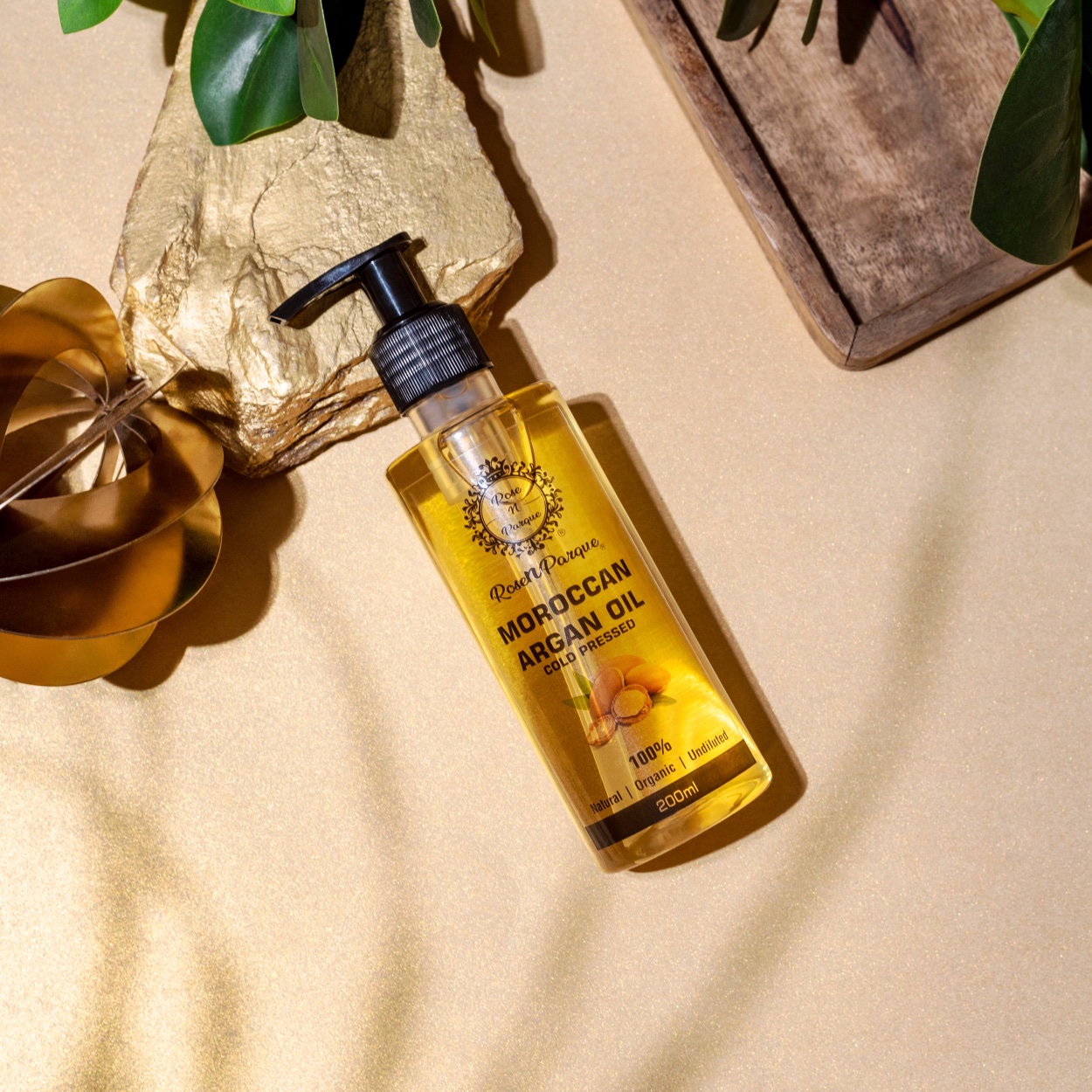 Transparent bottle of Moroccan argan oil with a pump dispenser on a gold surface.