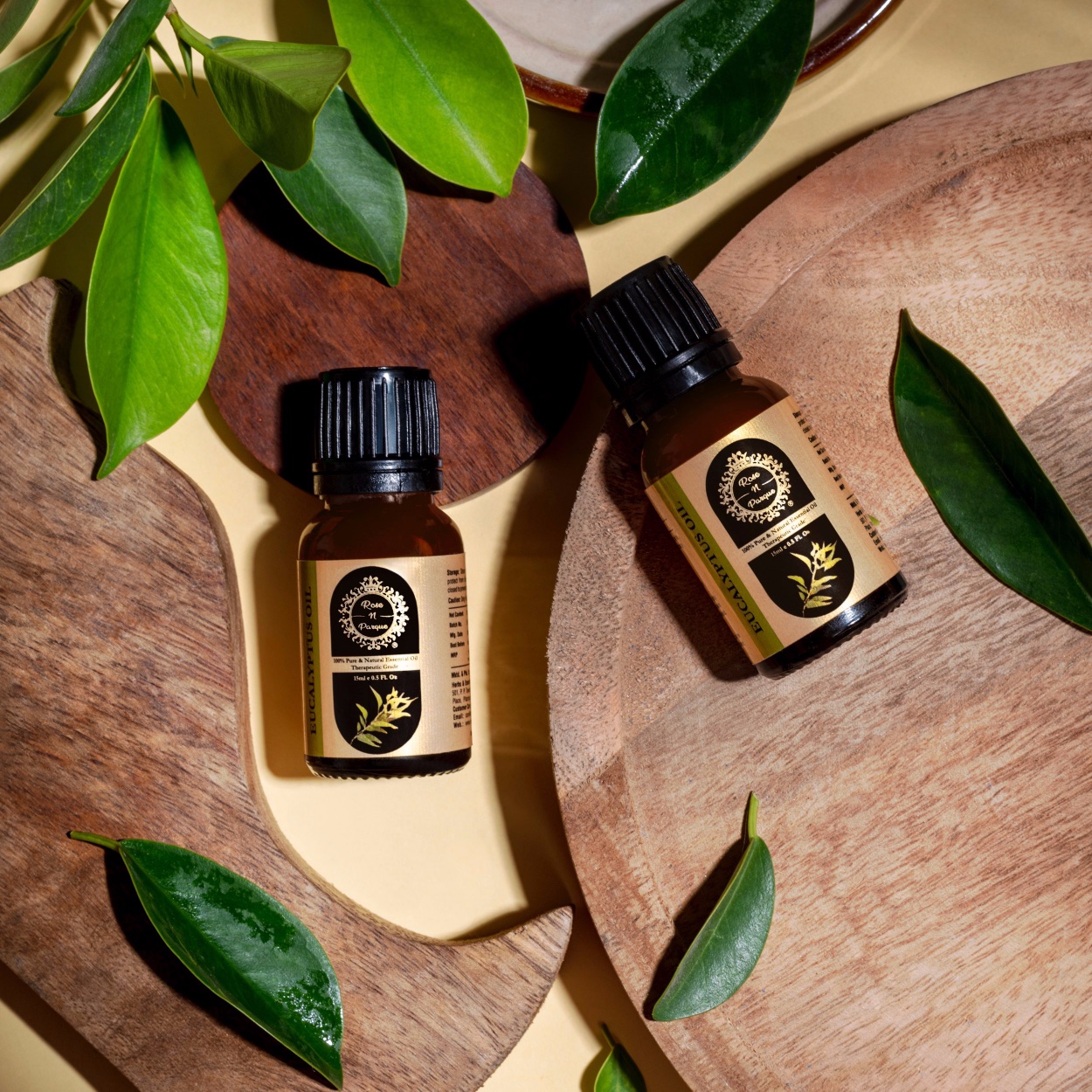Two brown glass bottles of essential oil placed on a wooden surface with green leaves.