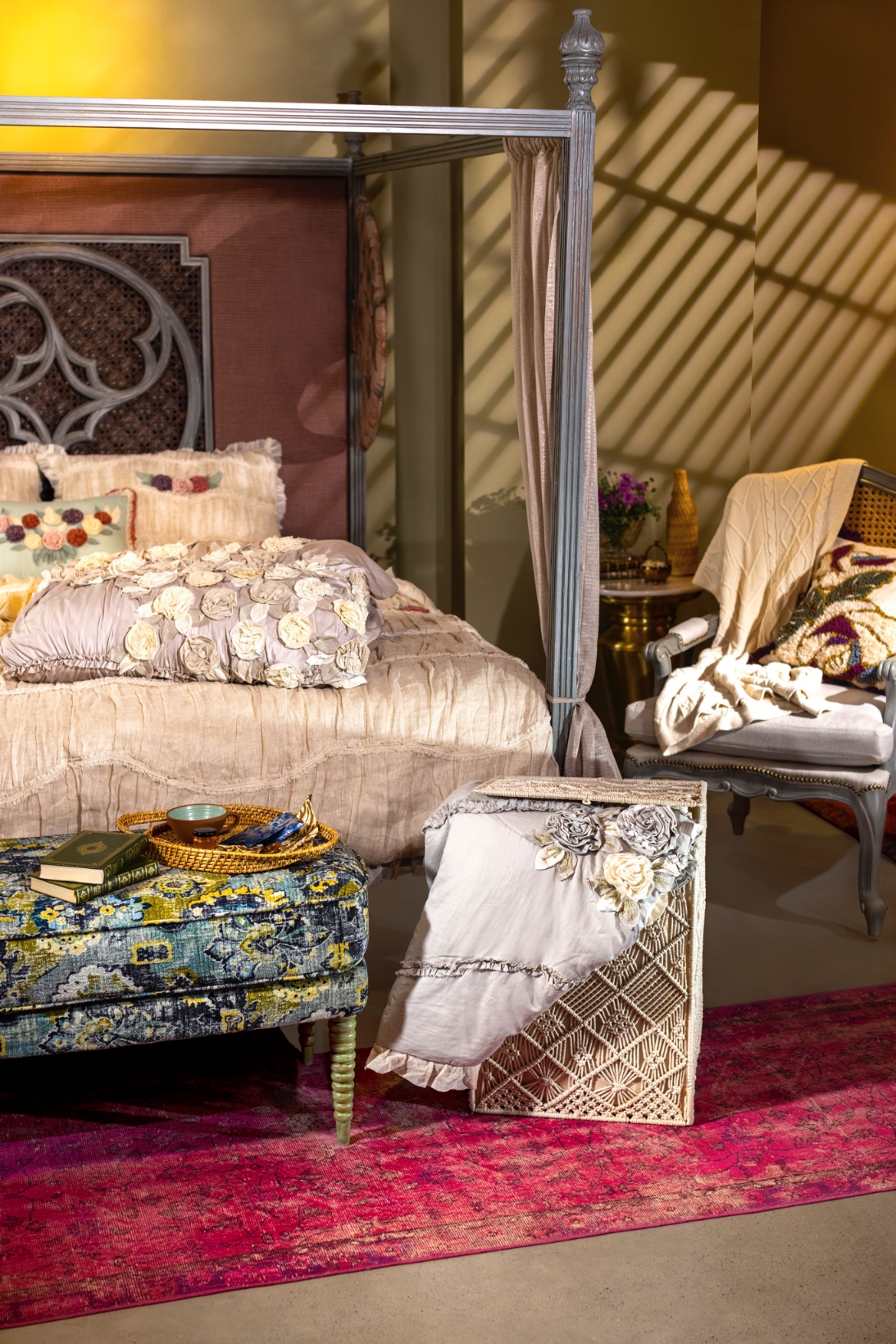 A beautifully arranged bedroom featuring a canopy bed, decorative pillows, and a patterned ottoman.