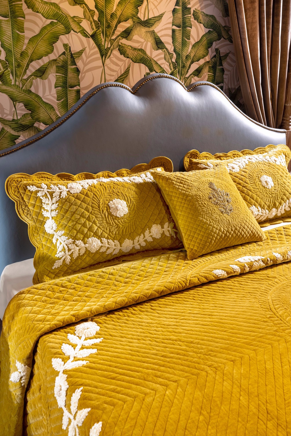 Yellow quilted bedding set featuring intricate embroidery and decorative pillows on a bed.