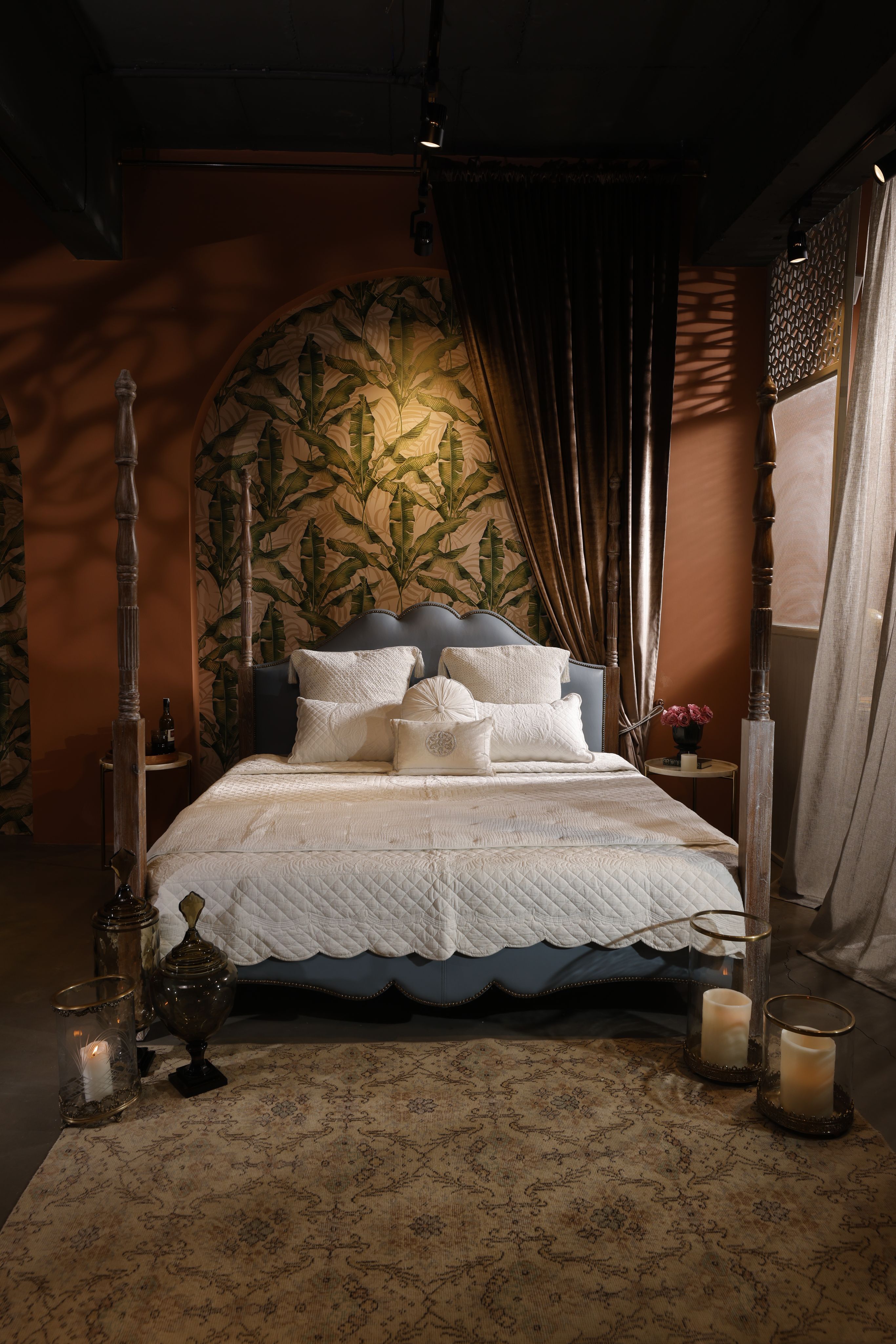A stylish bedroom featuring a canopy bed with white bedding and decorative pillows, surrounded by candles and a patterned rug.