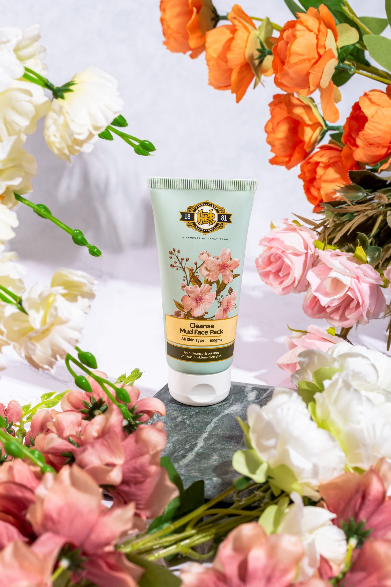 Tube of Cleanse Mud Face Pack with floral design surrounded by artificial flowers.