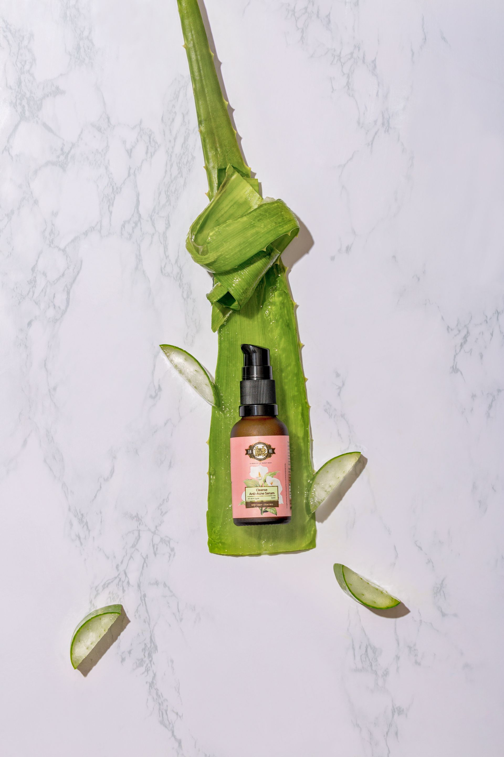 Aloe vera leaf with a pink skincare bottle positioned in the center and sliced aloe pieces around it.