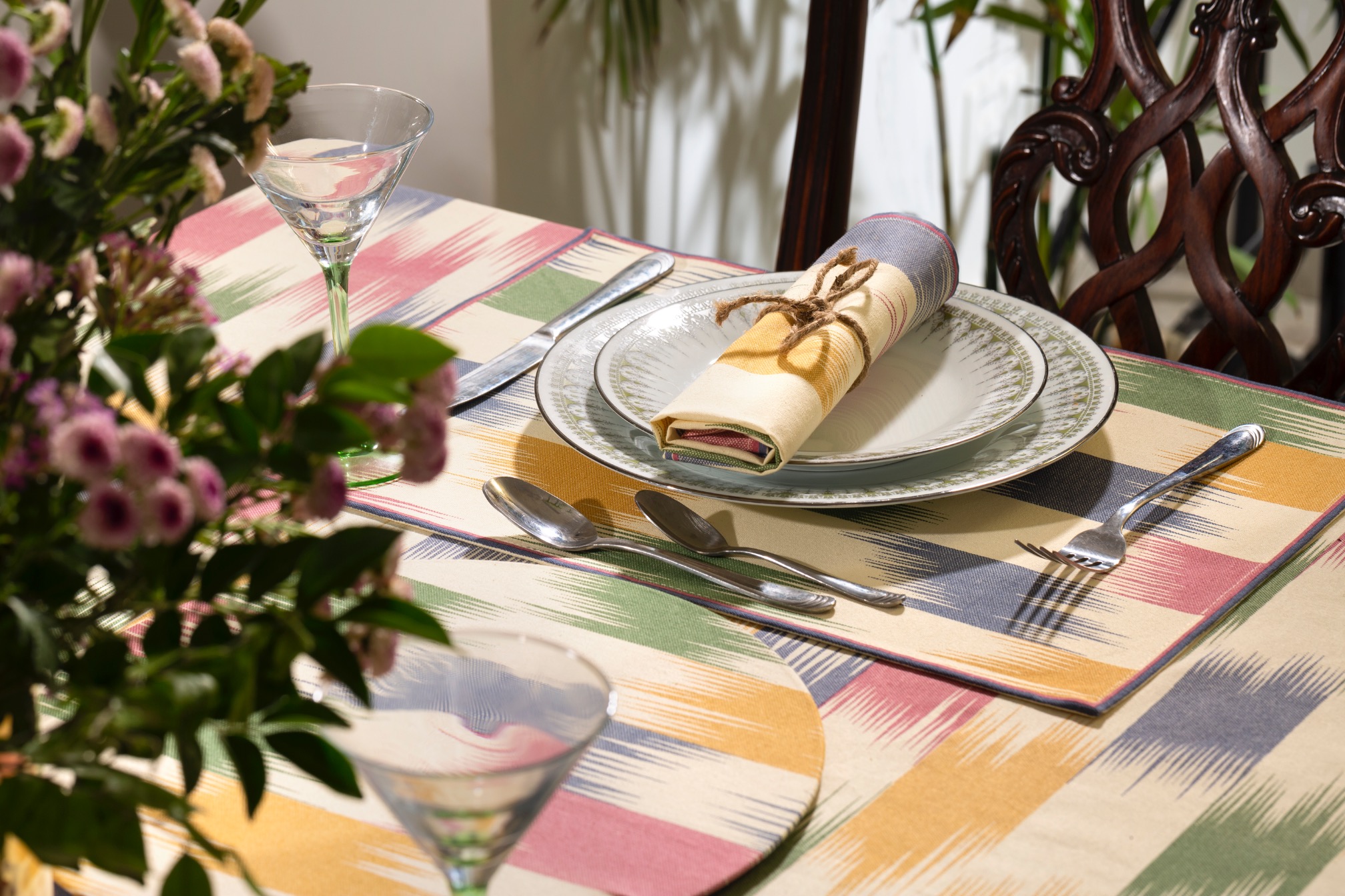 A table set with colorful tableware, including plates, napkins, and glasses, alongside a floral arrangement.