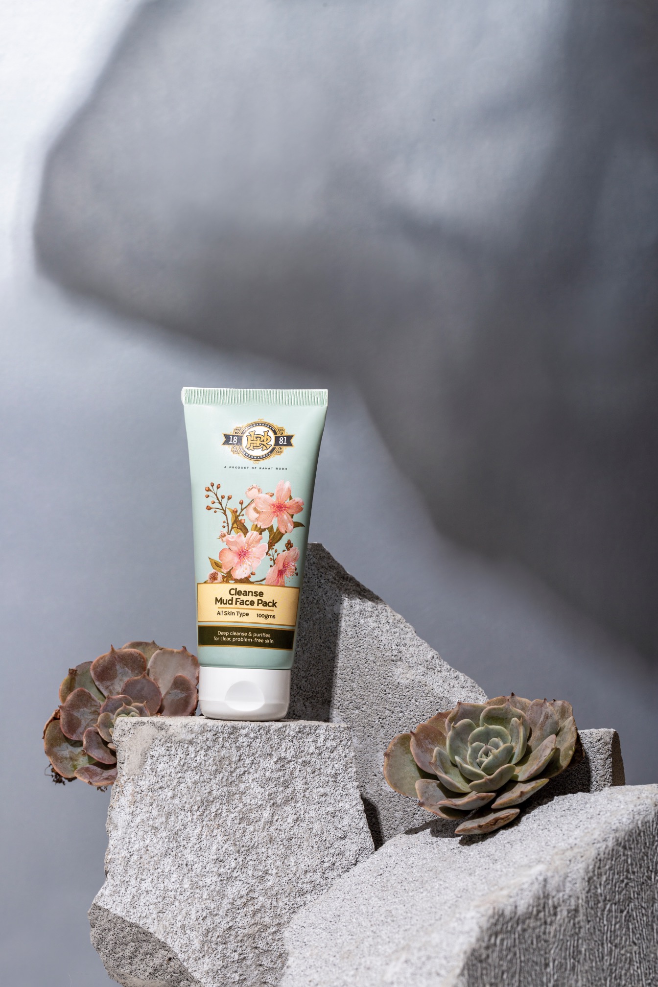 Cleansing mud face pack in a tube with floral design placed on textured stones.