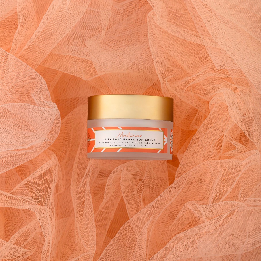 Container of Daily Love Hydration Cream with a gold lid on a textured background.
