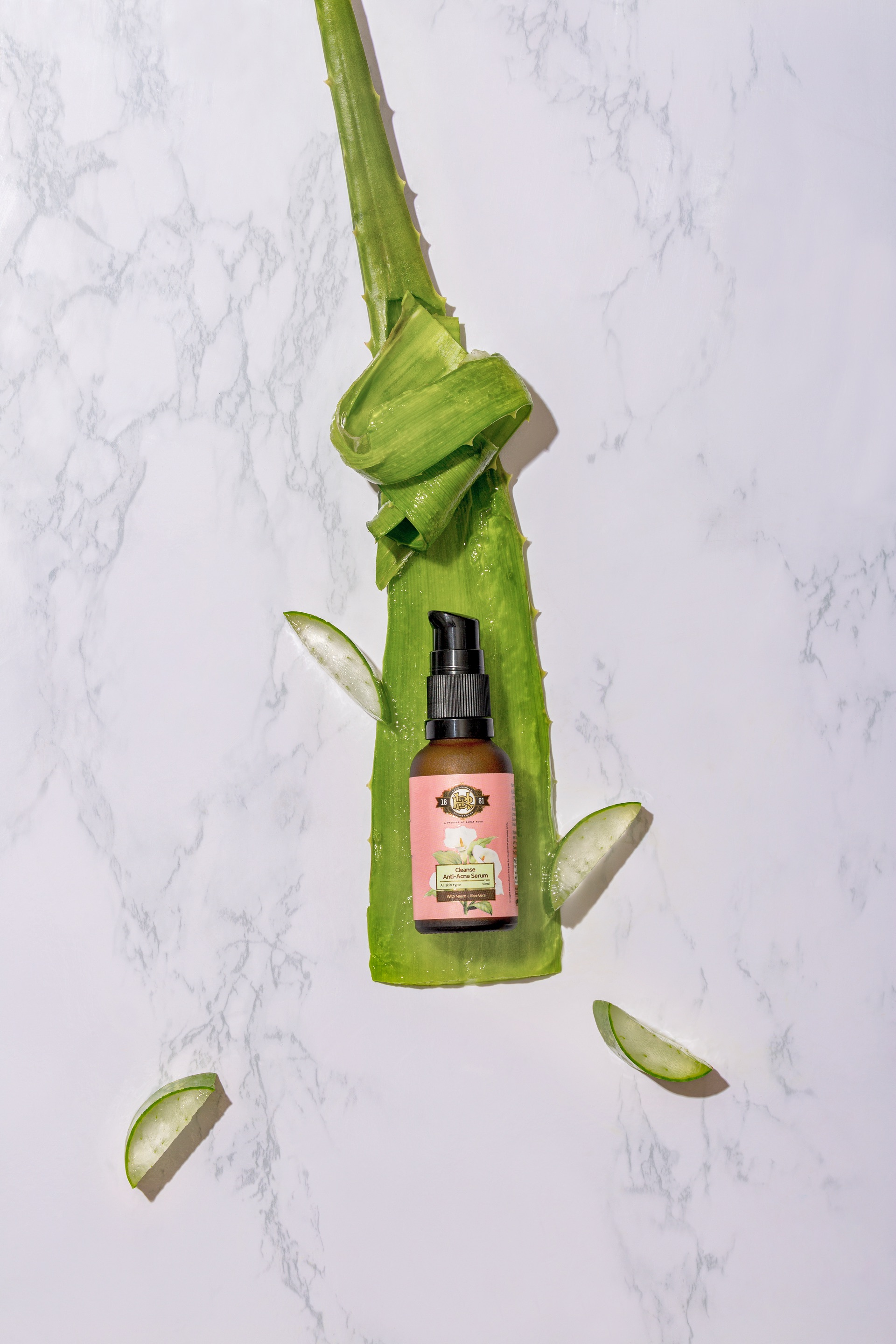 Aloe vera leaf with a pink skincare bottle positioned in the center against a marble background.