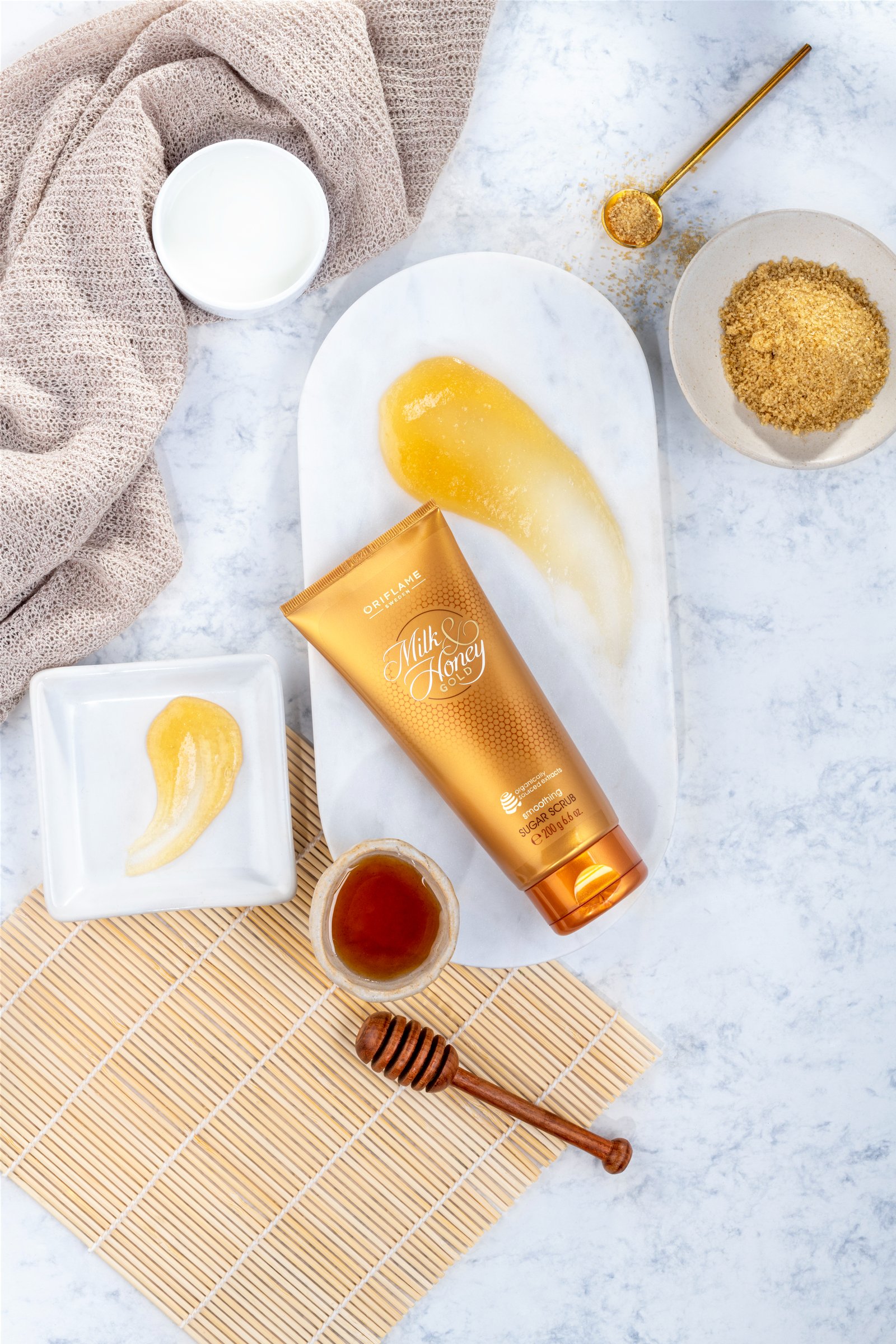 Oriflame Milk and Honey body cream tube placed on a marble surface with honey and sugar.