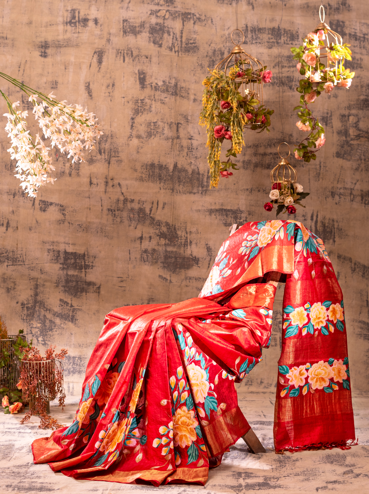 Red silk saree with floral patterns draped over a chair in a studio setting.