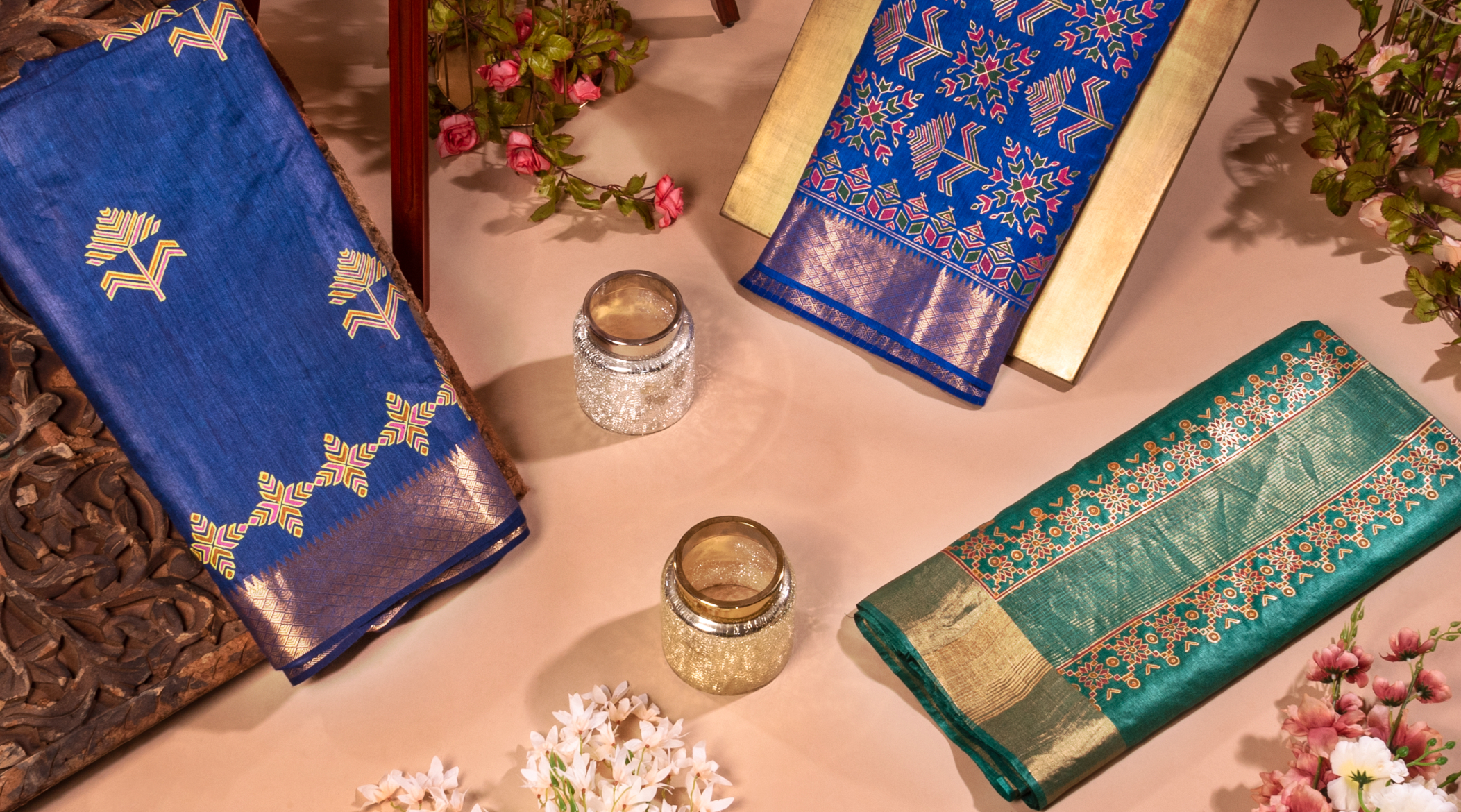 Three traditional Indian sarees in blue, green, and gold displayed with decorative elements.