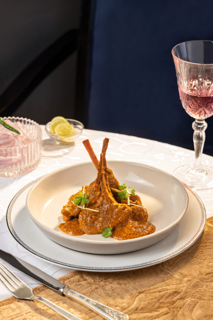 Delicious lamb chops served with a rich, spicy sauce, garnished with fresh herbs, on a white plate with a glass of red wine.