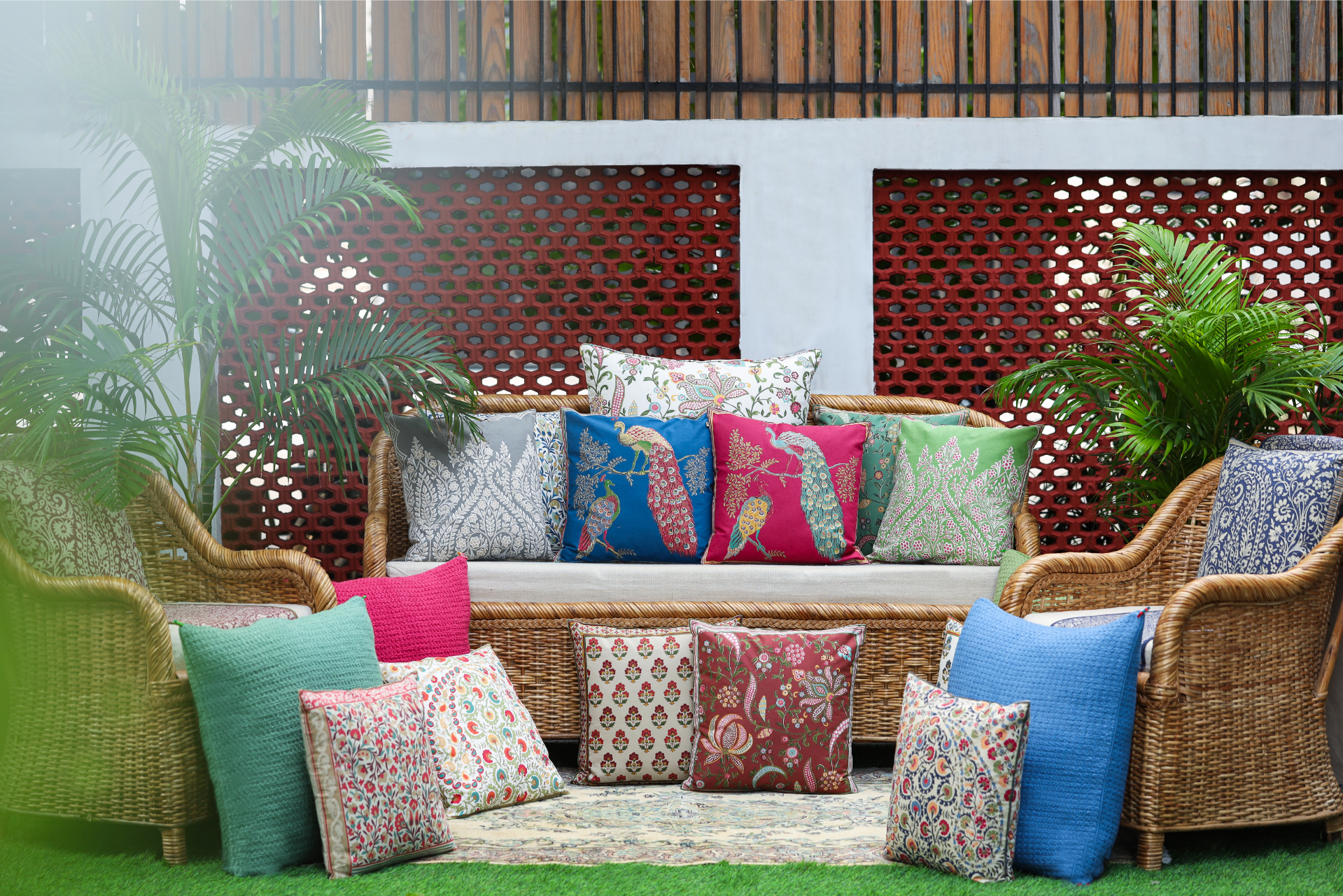 A collection of vibrant decorative cushions on a wicker sofa surrounded by greenery, showcasing various patterns and colors.