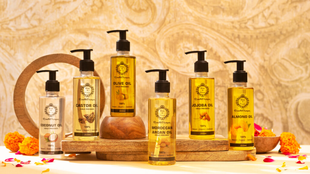 Bottles of different oils including coconut, castor, olive, jojoba, Moroccan argan, and almond oils arranged on a wooden display.