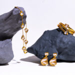 Gold jewelry including a necklace, earrings, and a bracelet displayed on gray rocks.