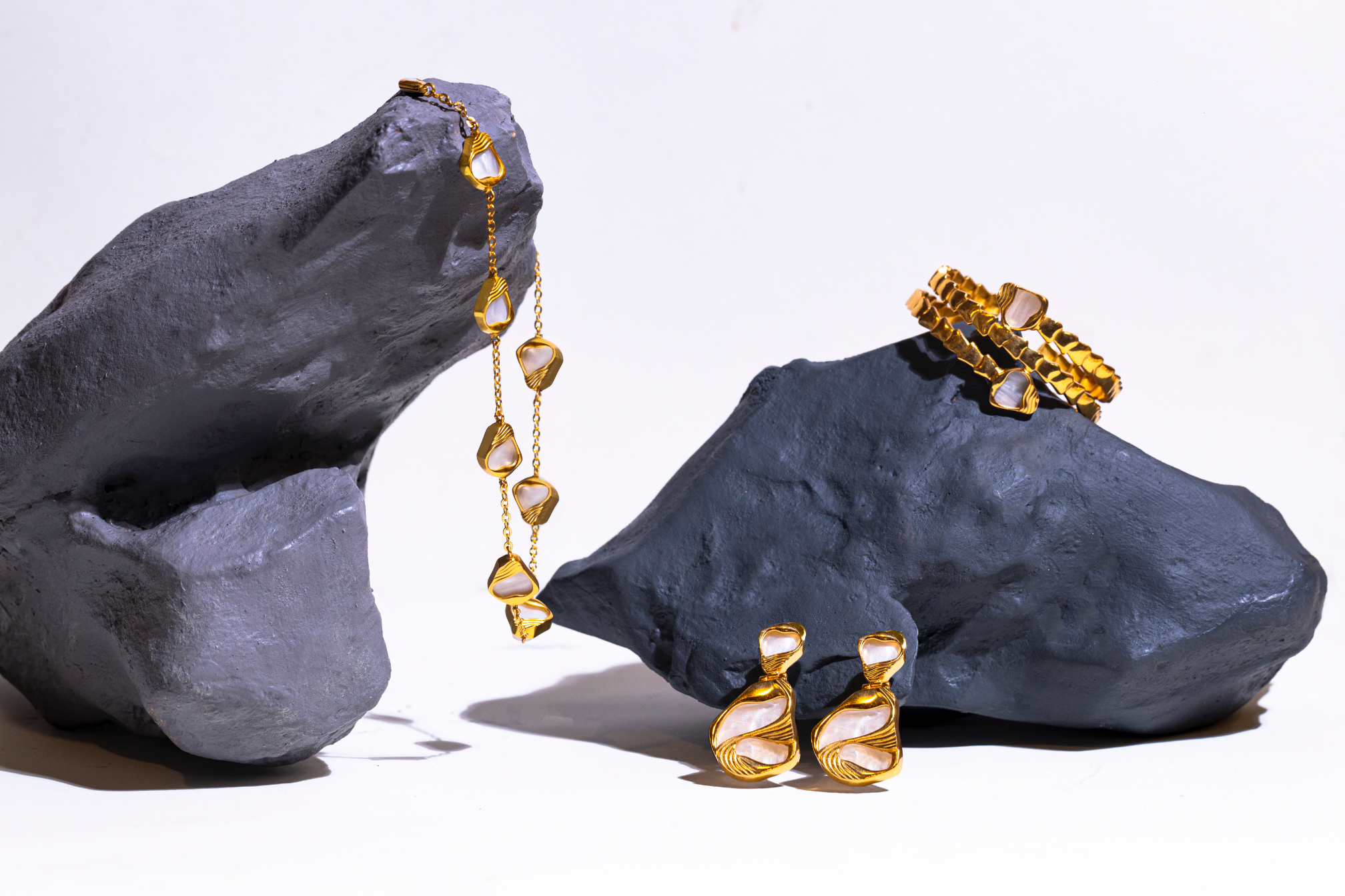 Gold jewelry including a necklace, earrings, and a bracelet displayed on gray rocks.