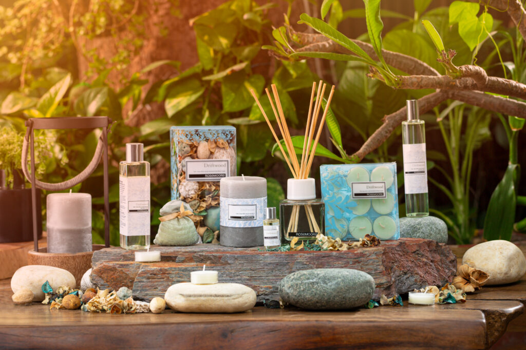 Various scented candles and diffusers arranged on a wooden surface with decorative stones and shells.