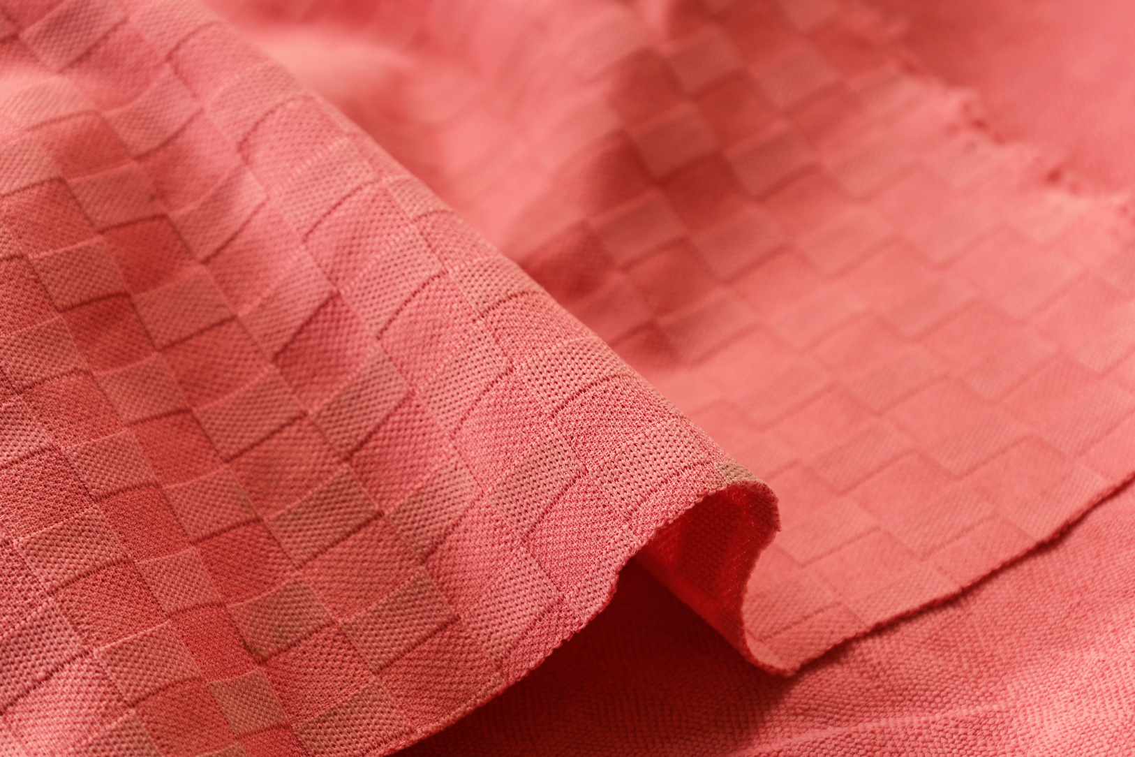 Close-up view of coral fabric with a woven square pattern and soft texture.