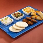 Assorted Indian snacks arranged on a blue platter with creamy dips, salad, fried pastries, croquettes, and flatbreads.